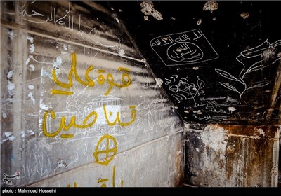 سمت راست تصویر پرچم داعش و سمت چپ دیوار نوشته دسته تک تیرانداز علی در شهر فلوجه