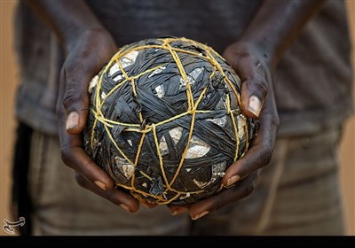 در این عکس که در سال 2017 گرفته شده است یک کودک مهاجر توپی دست‌ساز را در بین دستانش در کمپ آوارگان بیدی بیدی در شمال اوگاندا گرفته است. زمین های فوتبال و مسابقات بین روستایی در تمام کمپ های آوارگان دنیا قابل مشاهده است.
