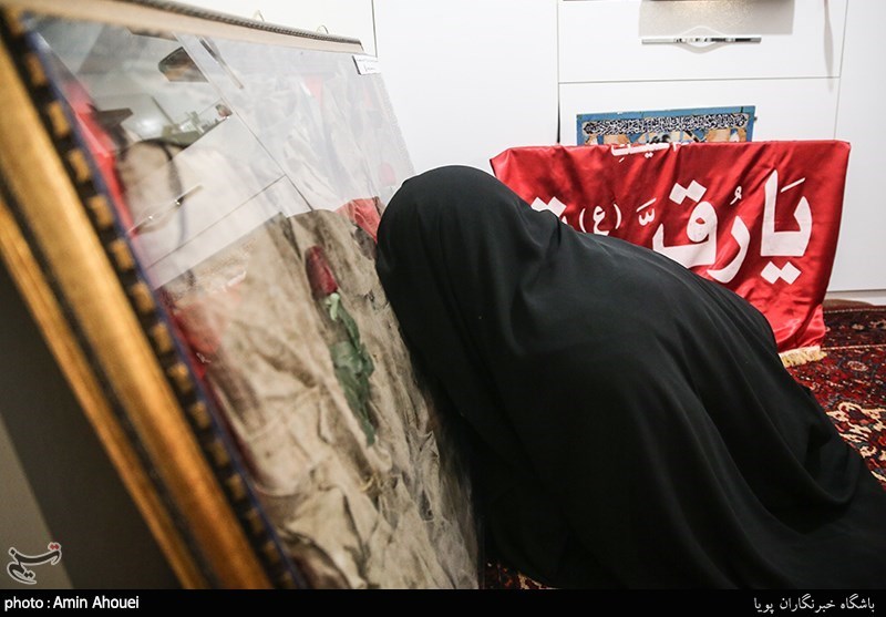 مادر شهید مدافع حرم جواد الله کرم در حال ادای احترام به لباس تفحص شده ی فرزندش