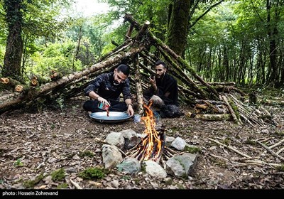  دو نفر از شرکت کنندگان در دوره زندگی در شرایط سخت و بقاء در طبیعت در حال درست کردن غذا در دل جنگل هستند.